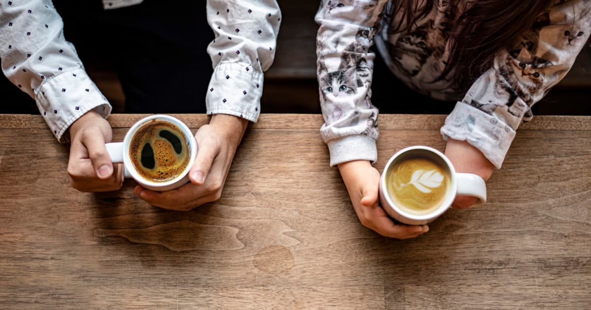 Deux personnes discutent autour d'un café à une table en bois