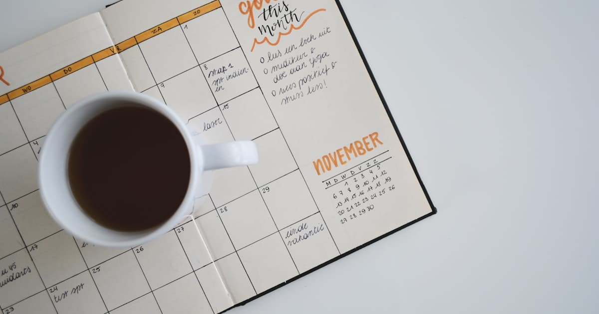 Un planning mensuel ouvert sur un bureau, avec une tasse de café